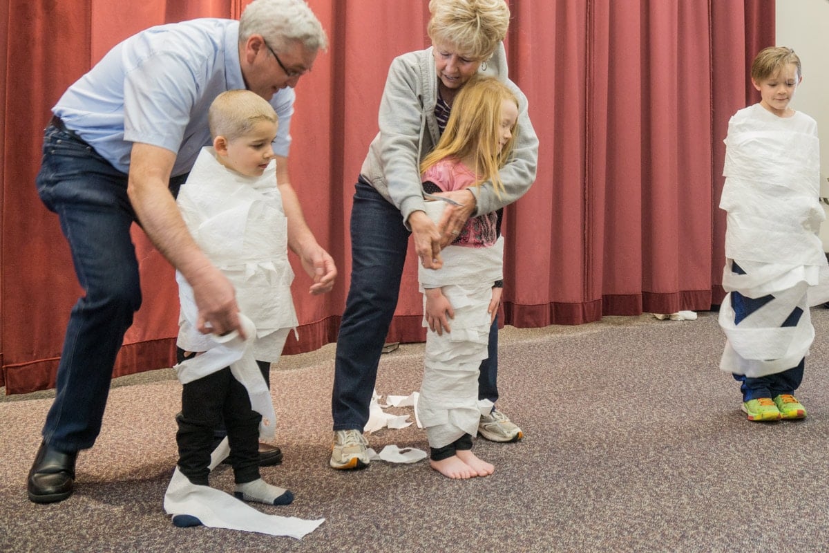 3 children being wrapped up like mummies with toilet paper.