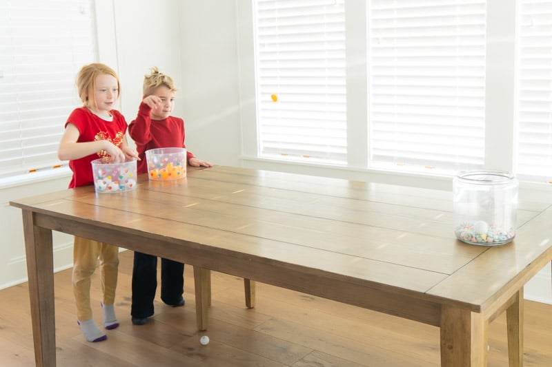 2 children bouncing ping pong balls into a bucket.